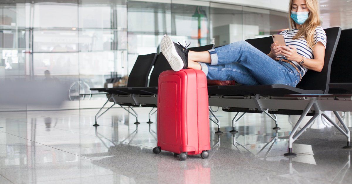 A woman wearing a mask sits and waits at an empty departure gate.