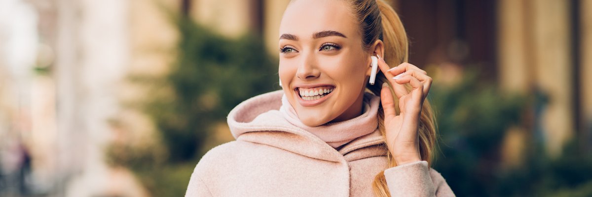 Woman with AirPods in ear smiling while walking outdoors.
