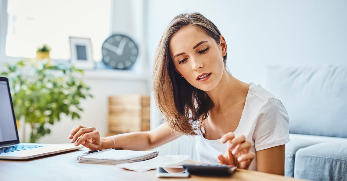 A woman sitting in her living room with a calculator, notebook, and laptop on the coffee table.