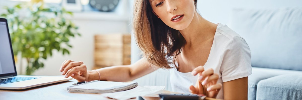 A woman sitting in her living room with a calculator, notebook, and laptop on the coffee table.