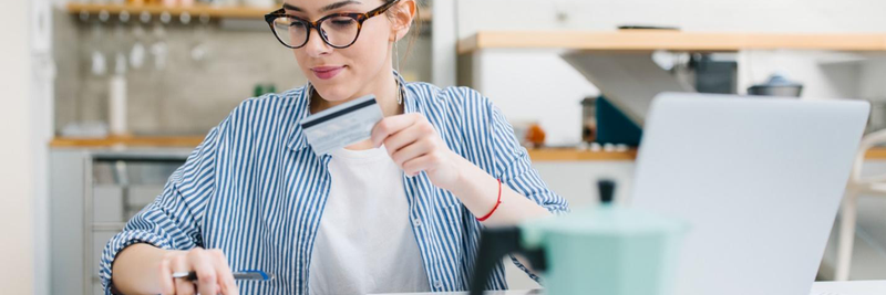 woman sitting at table with laptop, credit card, calculator, and coffee