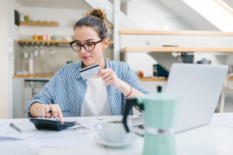 woman sitting at table with laptop, credit card, calculator, and coffee