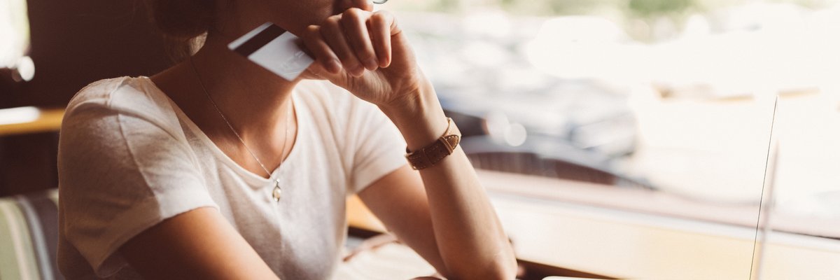 A woman sitting in front of her laptop holding a credit card and looking worried.
