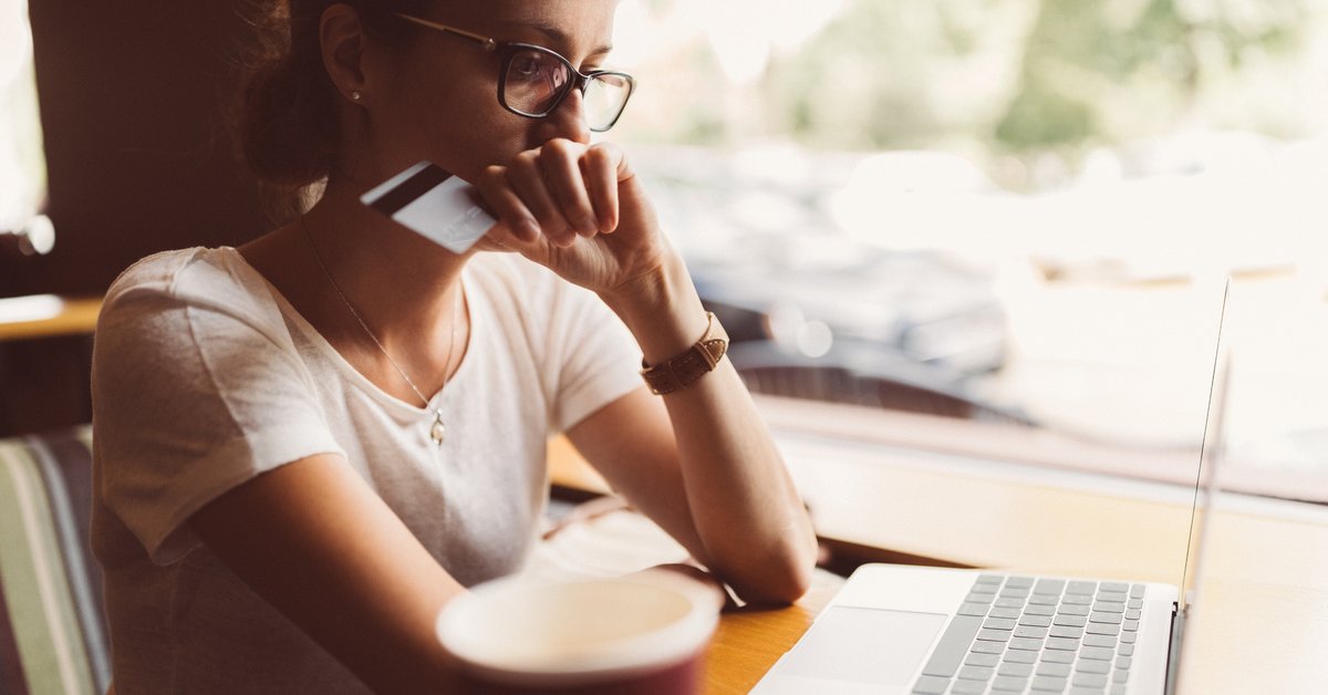 A woman sitting in front of her laptop holding a credit card and looking worried.