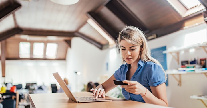 A woman sitting at a table in her home and typing on her laptop while holding her credit card.