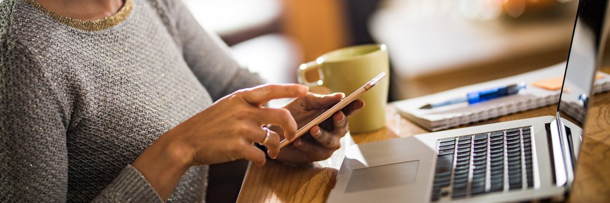 A woman dialing a number on her phone and sitting at a table with her laptop.
