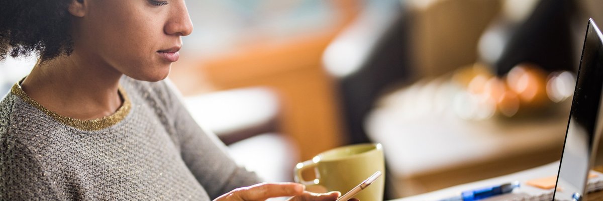 A woman dialing a number on her phone and sitting at a table with her laptop.