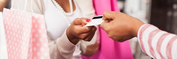 A woman holding pink shopping bags handing her credit card to the cashier in a clothing store.