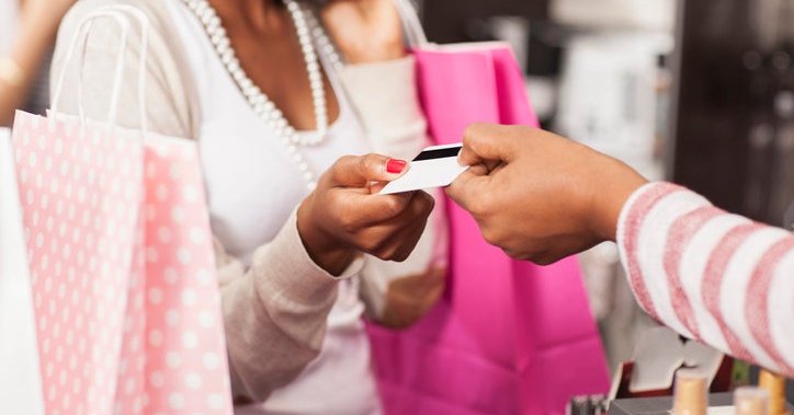 A woman holding pink shopping bags handing her credit card to the cashier in a clothing store.