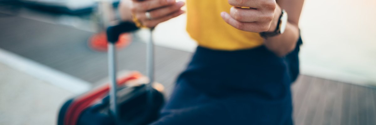 A female traveler sitting with a suitcase and holding a credit card and phone.
