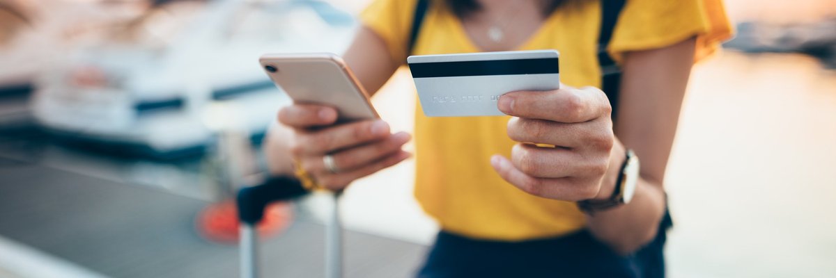 A female traveler sitting with a suitcase and holding a credit card and phone.
