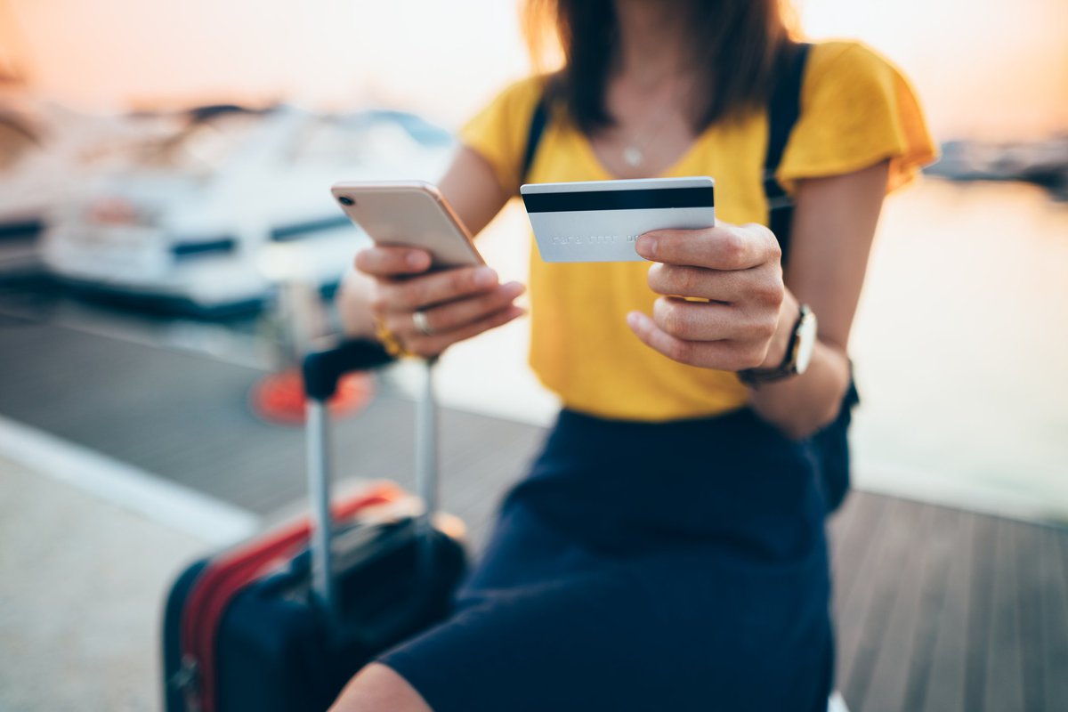 A female traveler sitting with a suitcase and holding a credit card and phone.