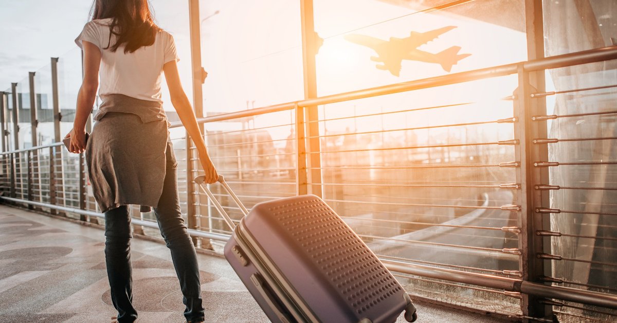 A female traveler walking through a sunny airport with her suitcase.