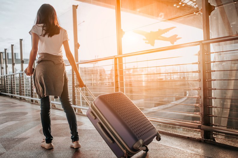 A female traveler walking through a sunny airport with her suitcase.