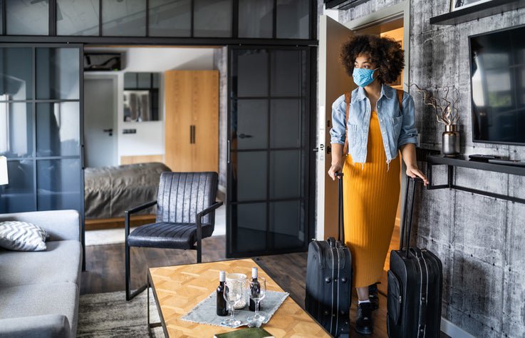 A woman in a medical mask rushes her two suitcases to a comfortable hotel room.