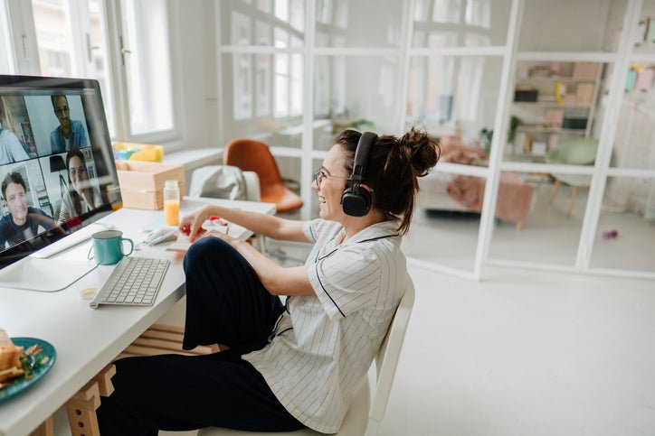 A woman wearing headphone and sitting at a desk in her apartment having a video call with coworkers.