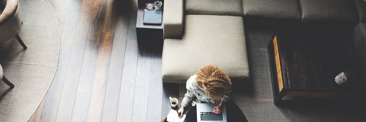 A woman sitting on the floor of her living room with her cat while working on her laptop.