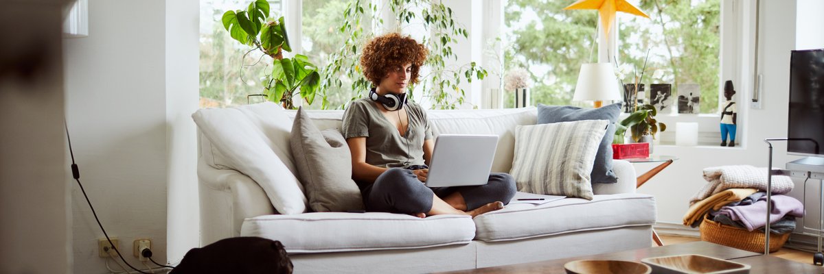 A woman sitting cross-legged on the couch working on her laptop.