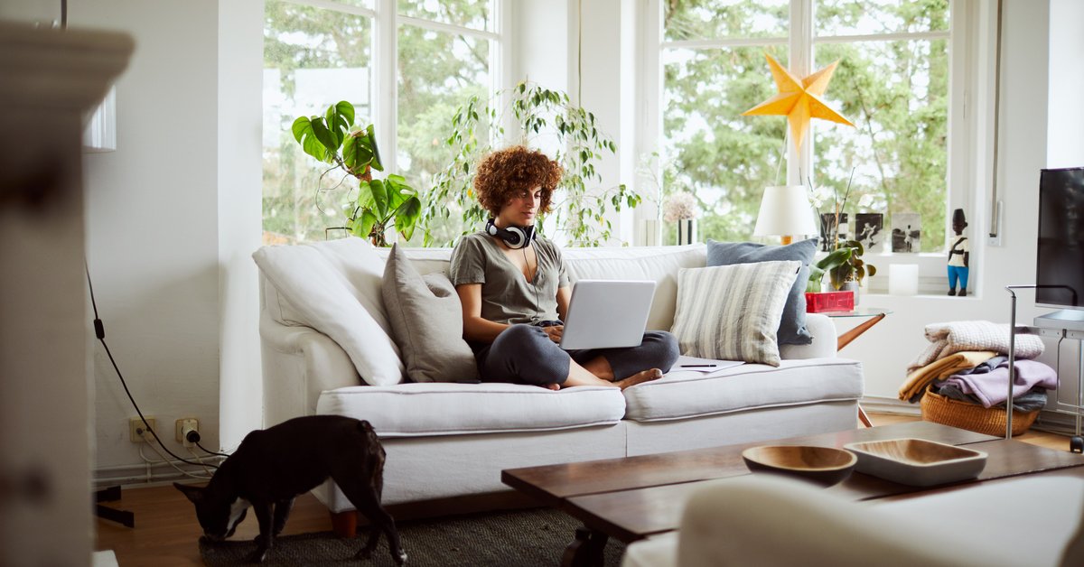 A woman sitting cross-legged on the couch working on her laptop.