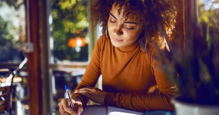 A woman sitting at a sunny table and writing in a notebook.