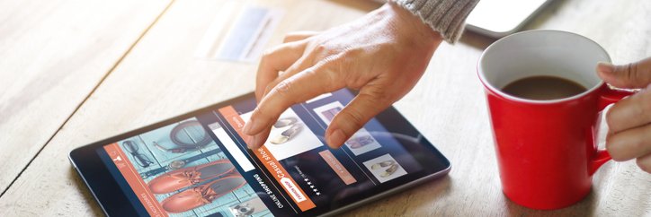 A woman's hand hovering over a tablet open to an online shopping window.