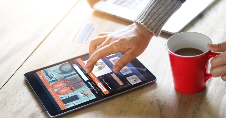 A woman's hand hovering over a tablet open to an online shopping window.