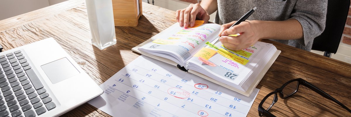 A women sitting at a sunny desk with a laptop, calendar, and planner.
