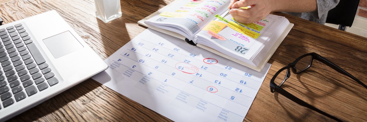A women sitting at a sunny desk with a laptop, calendar, and planner.
