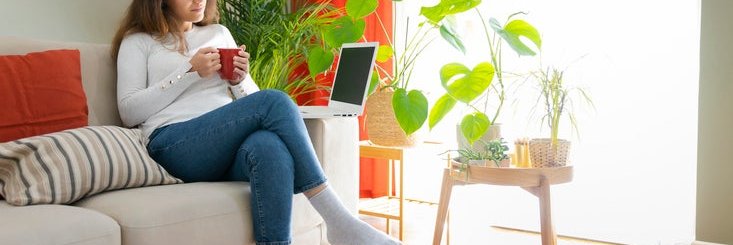 A woman on the couch with a hot beverage and a laptop.