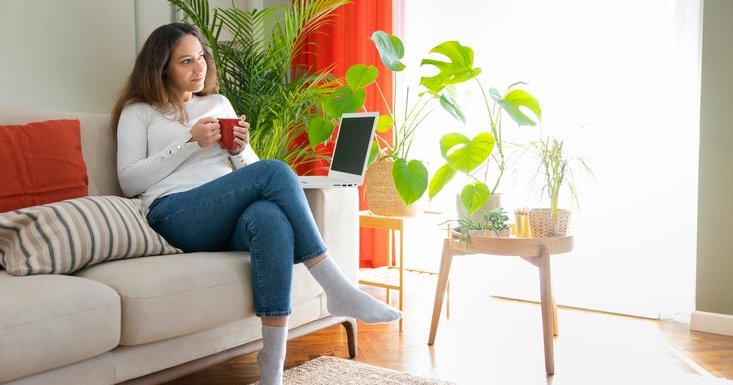 A woman on the couch with a hot beverage and a laptop.