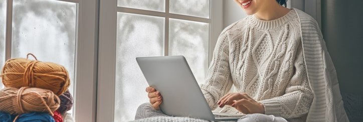 A woman working on her laptop by a window in her home.