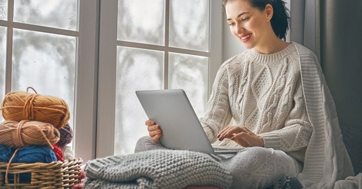 A woman working on her laptop by a window in her home.