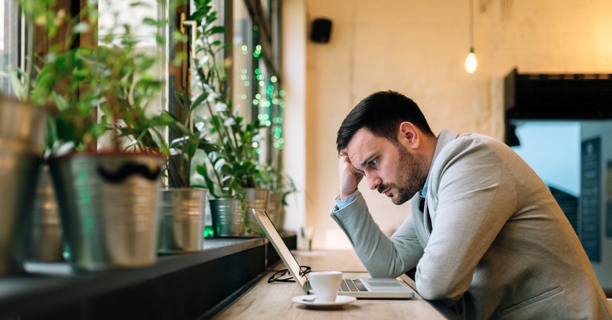 A worried-looking man looking at a laptop in a cafe.