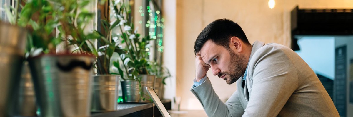 A worried-looking man looking at a laptop in a cafe.