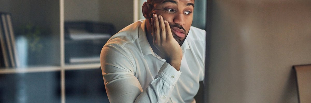 A worried-looking man staring at his computer with his chin in his hand.