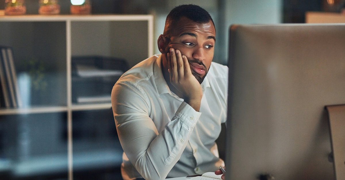 A worried-looking man staring at his computer with his chin in his hand.