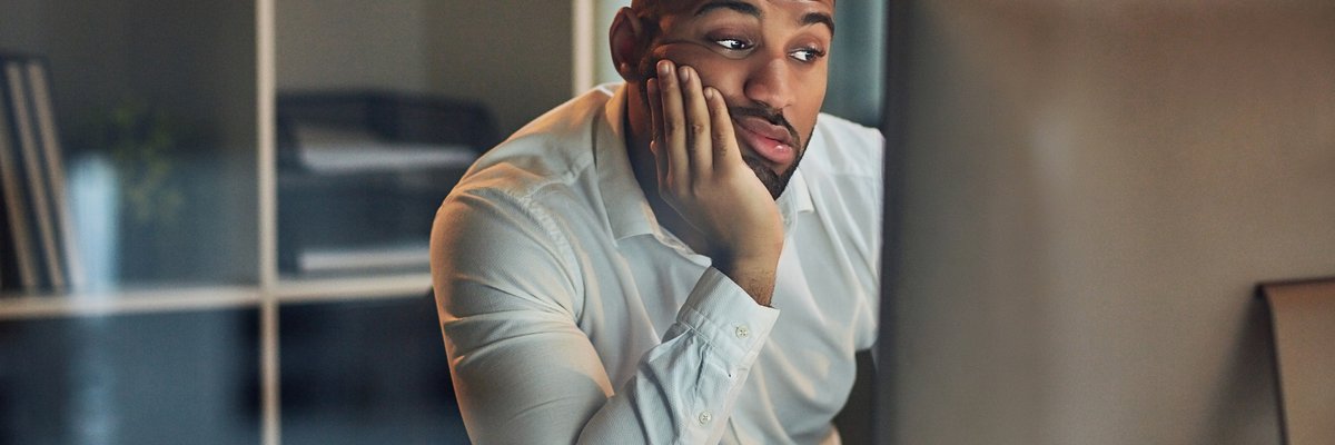 A worried-looking man staring at his computer with his chin in his hand.