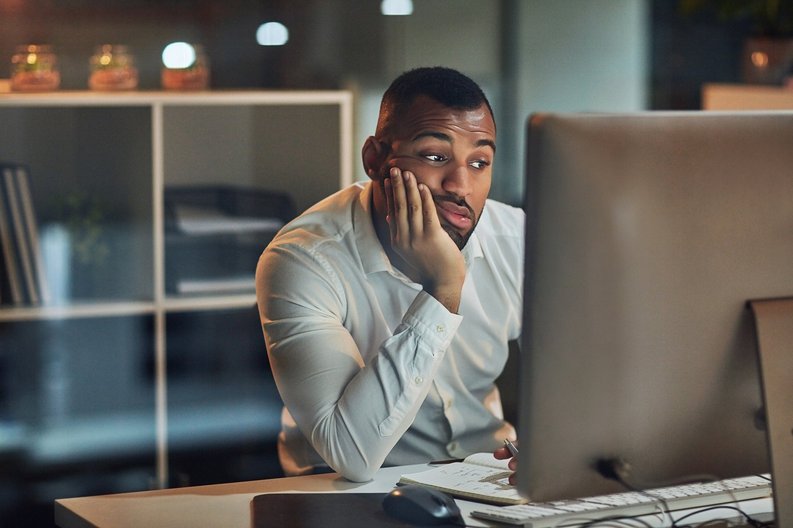 A worried-looking man staring at his computer with his chin in his hand.