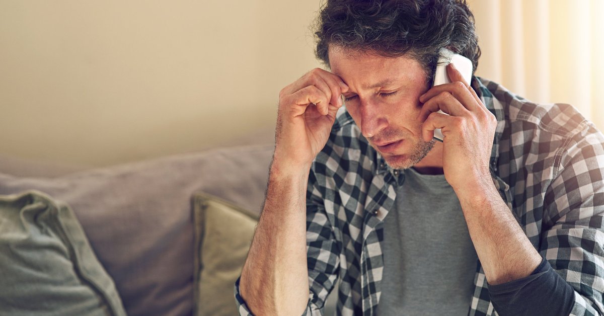 A man looking worried while on a phone call sitting on his couch.