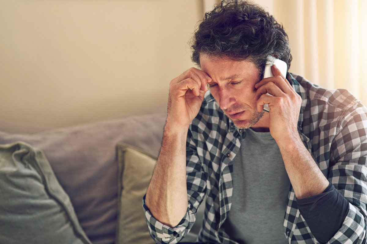 A man looking worried while on a phone call sitting on his couch.