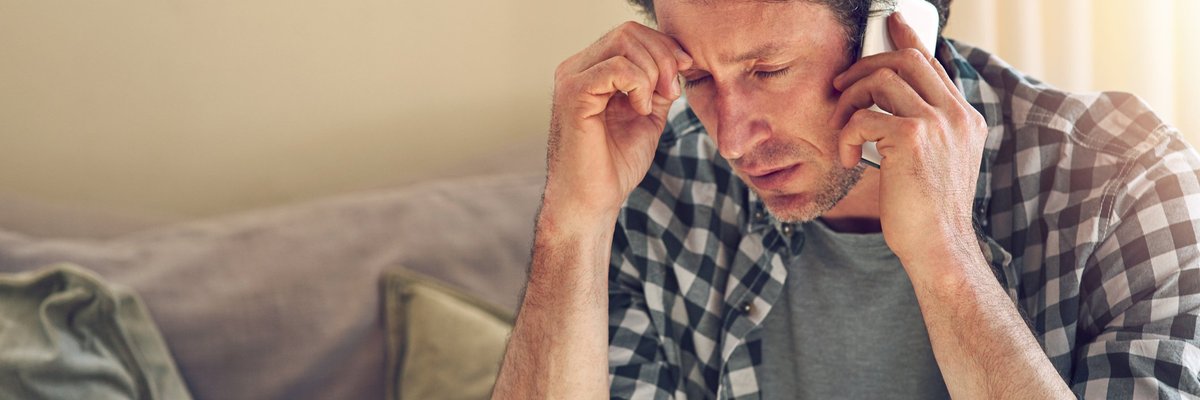 A man looking worried while on a phone call sitting on his couch.