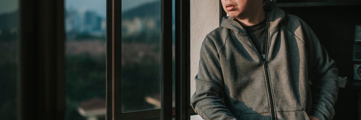 A worried person looking out the window of their apartment.