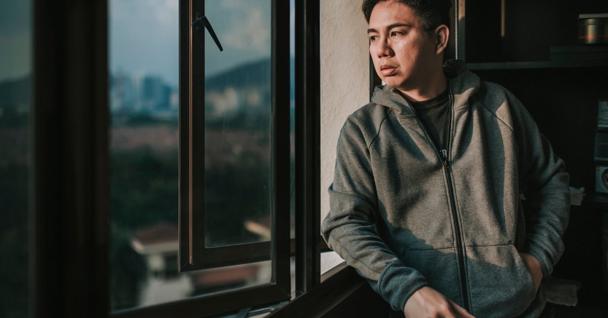 A worried person looking out the window of their apartment.