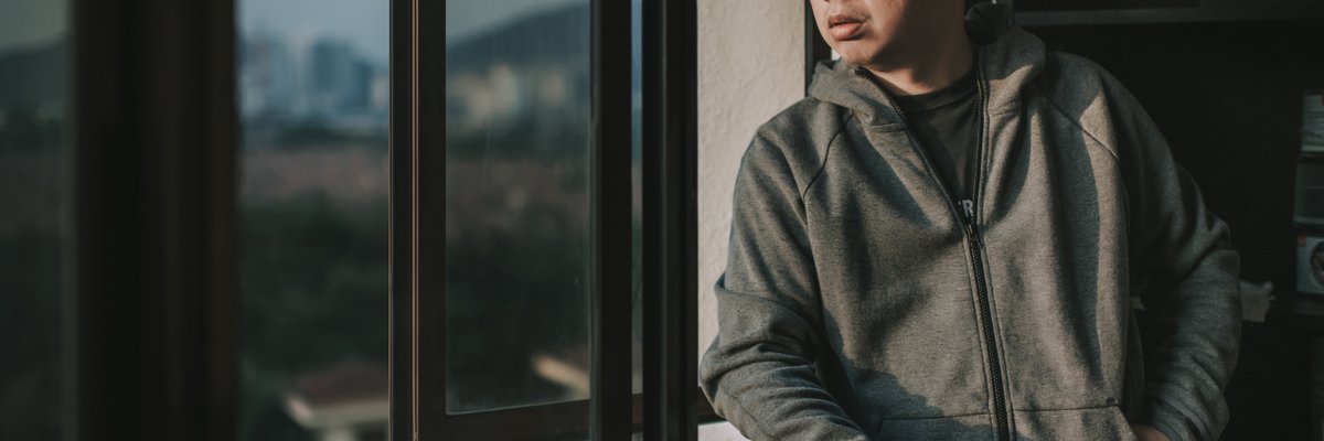 A worried person looking out the window of their apartment.