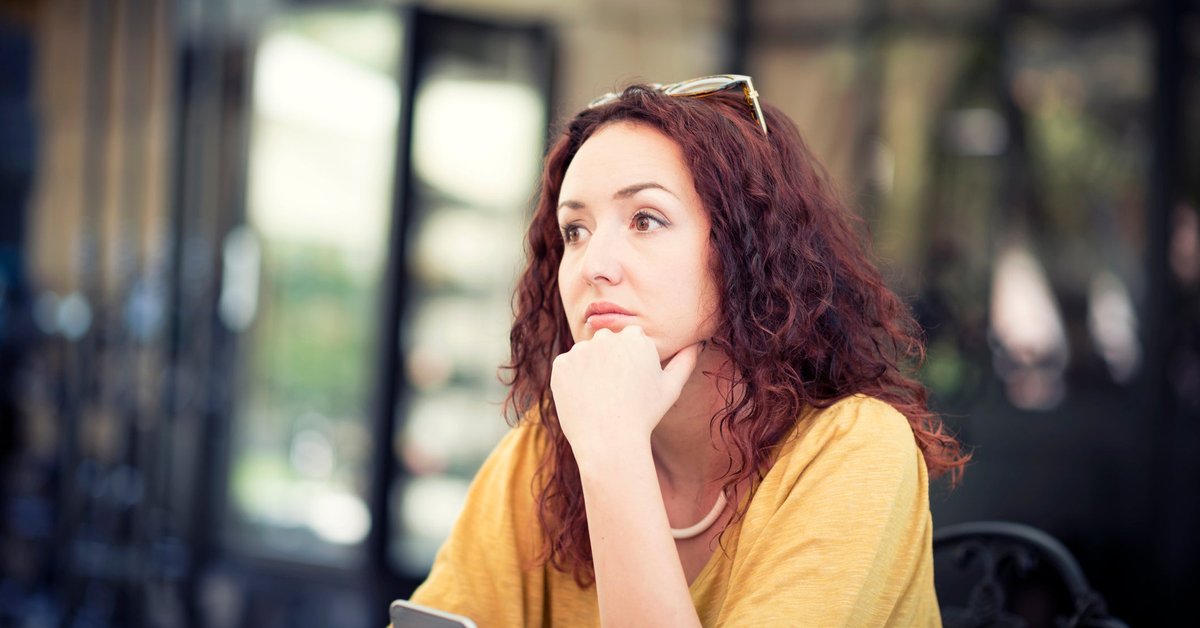 A worried person sitting with their chin resting on their hand and staring off into the distance.