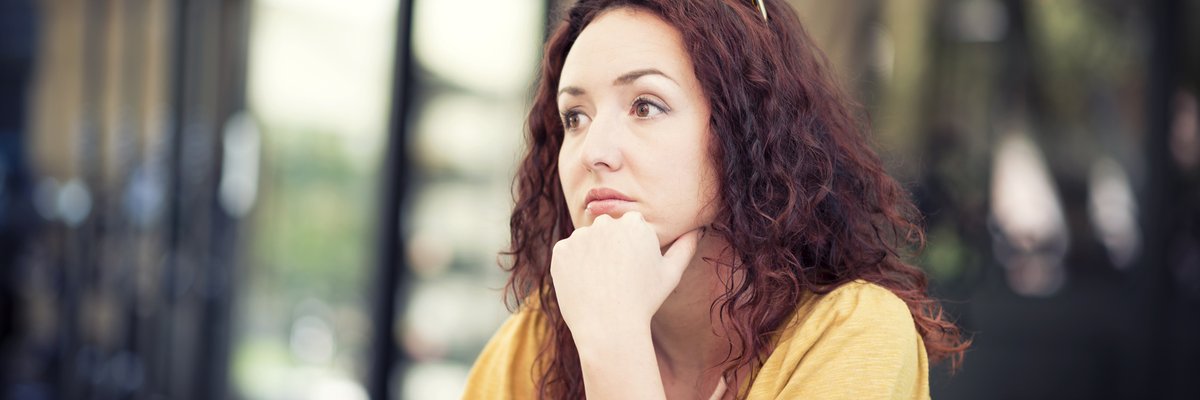 A worried person sitting with their chin resting on their hand and staring off into the distance.