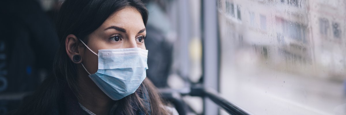 A worried-looking woman wearing a protective mask while riding the bus.