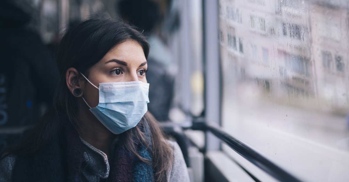 A worried-looking woman wearing a protective mask while riding the bus.