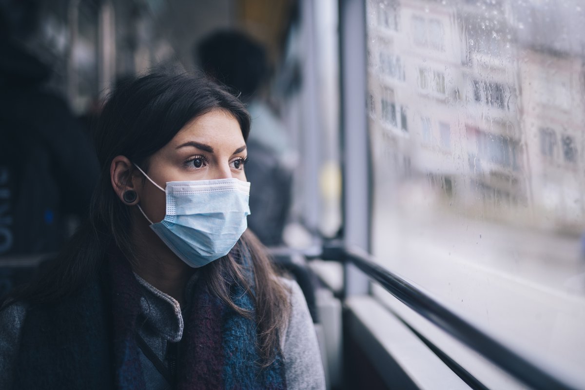 A worried-looking woman wearing a protective mask while riding the bus.