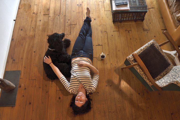 Upset women laying on the wood floor of her living room and petting her dog.